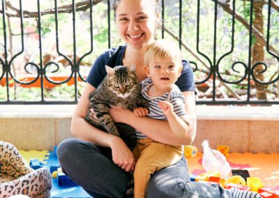 Mom sits on a rug on the balcony and holds a small child and a cat on her lap. High quality photo
